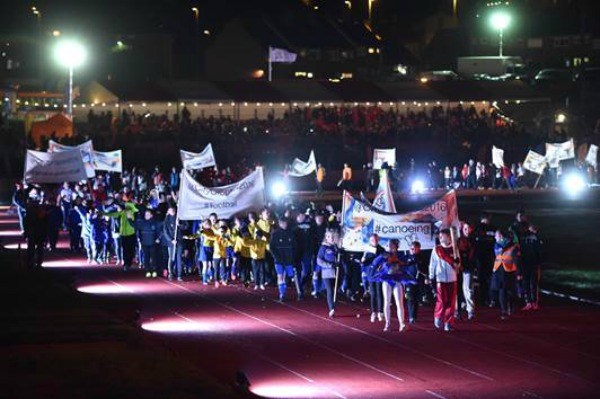 athletics event opening ceremony with teams waving banners walking along the running track waving